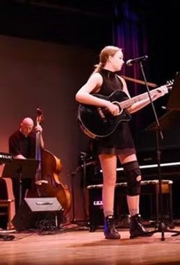 A student singing and playing guitar on stage